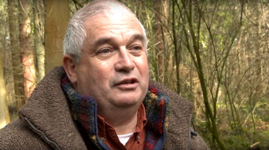 A man wearing a thick coat in woodland talking to the camera