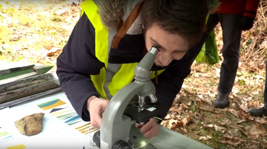Visitor in hi-vis jacket looks at soil through a microscope