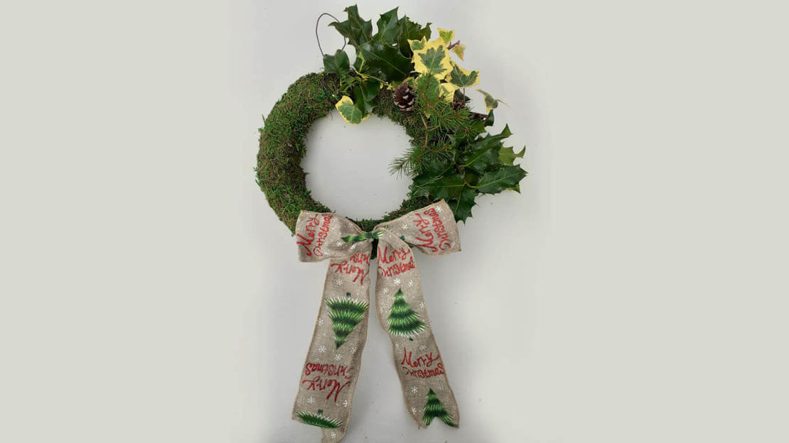 Wreath base with one quarter covered in foliage and Christmas ribbon at the bottom