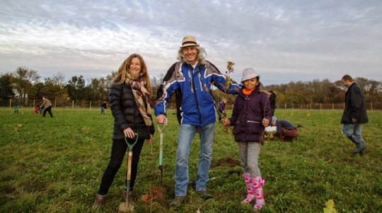 Family at community tree planting event posing for photo with spades and saplings