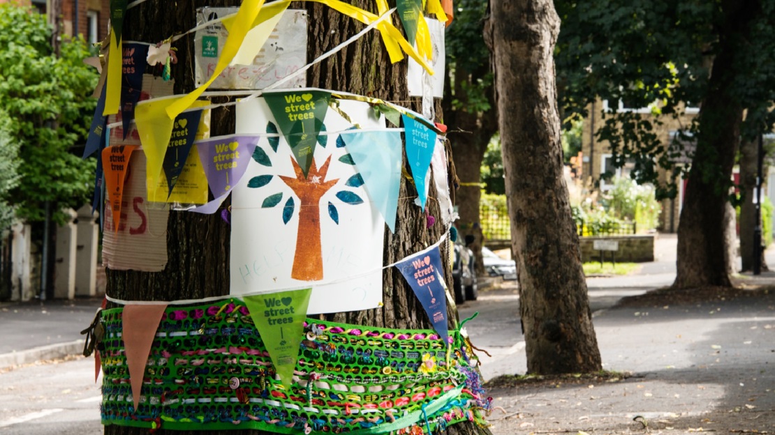 A roadside tree trunk decorated with bunting and pictures