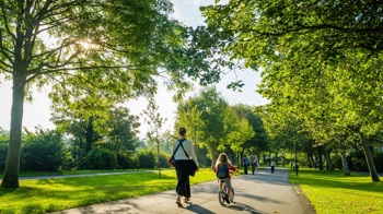 Woman walking with a child on a bicycle through a sunny park with lots of trees Woman walking with a child on a bicycle through a sunny park with lots of trees