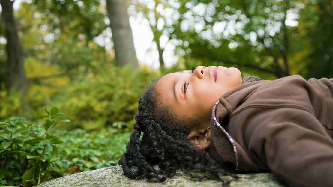 Girl lying on a rock looking up at the trees