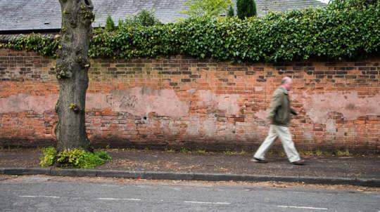 Man walking along pavement with street tree