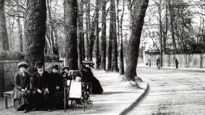 Black and white image of Victorian street with trees and people seated on bench