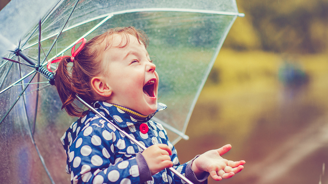 Little girl with an umbrella laughing in rain