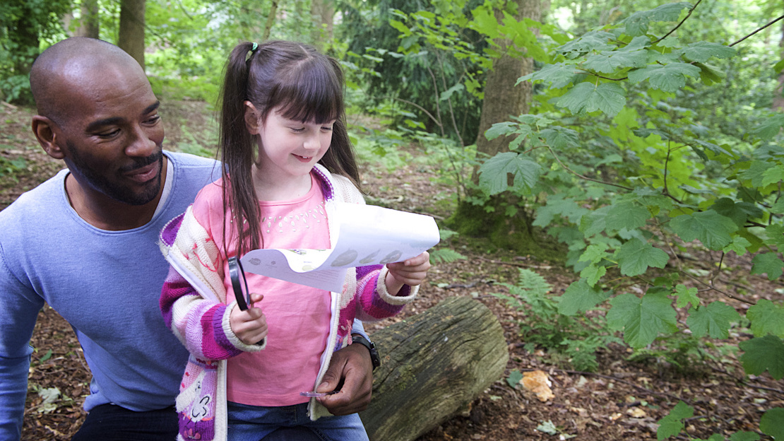 Father and daughter looking at paper with scavenger hunt in woods