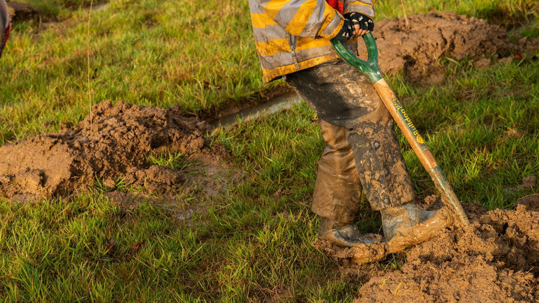 Muddy boots and spade while digging holes for tree planting.