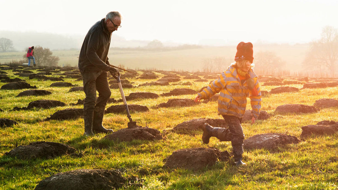 Man digging holes for saplings while a boy runs by him.