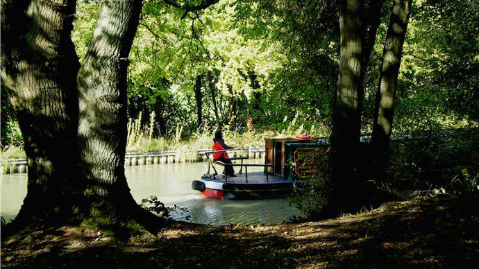 Canal boat passing shaded woodland clearing