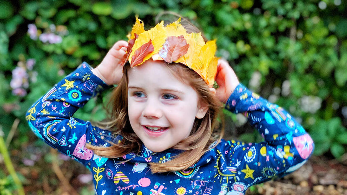 Smiling young girl wearing a crown made from yellow and brown leaves