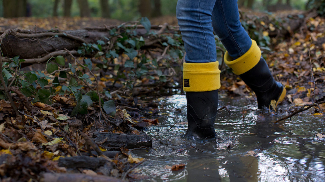 Lady in wellies walks through woodland puddle