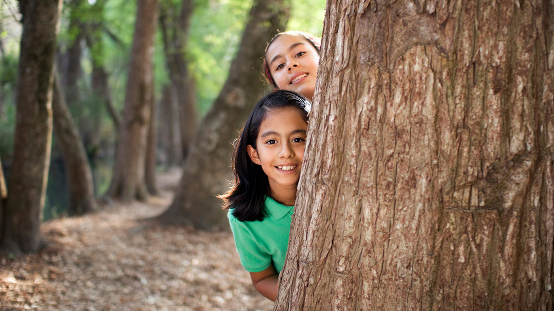 Girls playing and hiding behind tree