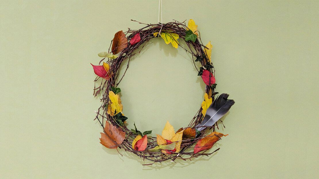 An autumn wreath hanging on a wall, made from birch twigs, fallen leaves and feathers
