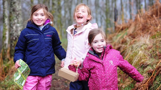 Three young children in coats with a map and collection box laughing