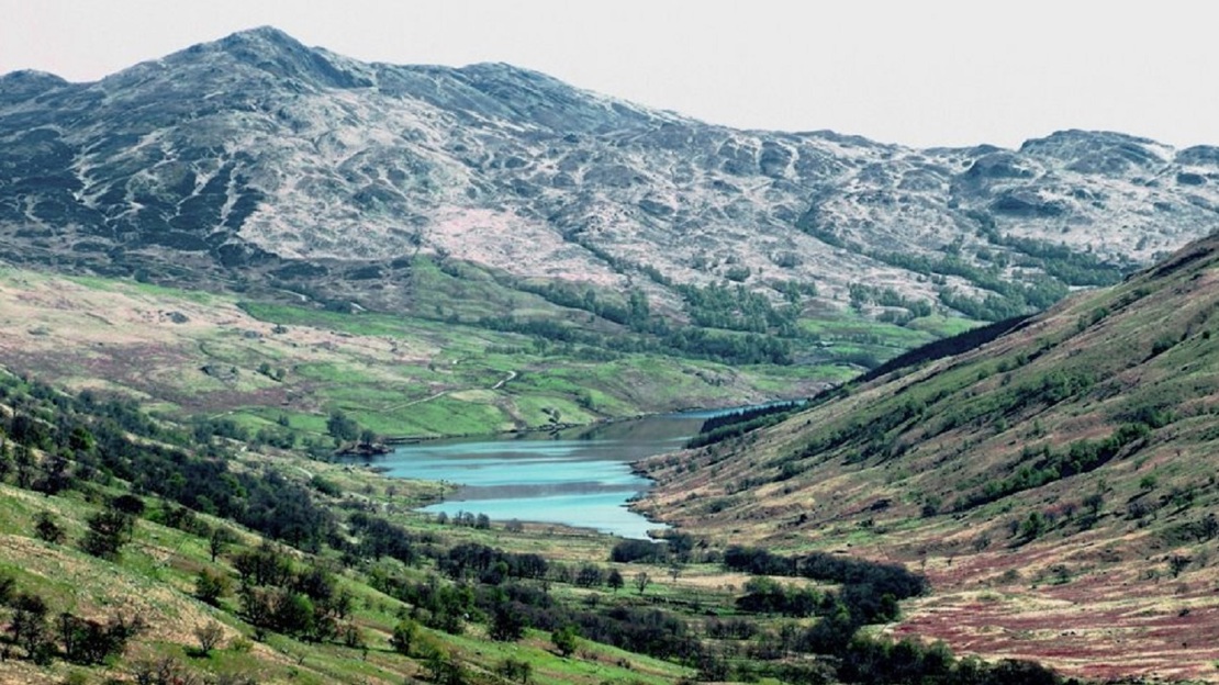 Landscape view of mountains, fields and lake with few trees and bare areas