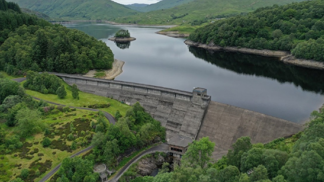Dam in the foreground with reservoir and tree-covered hills in the background