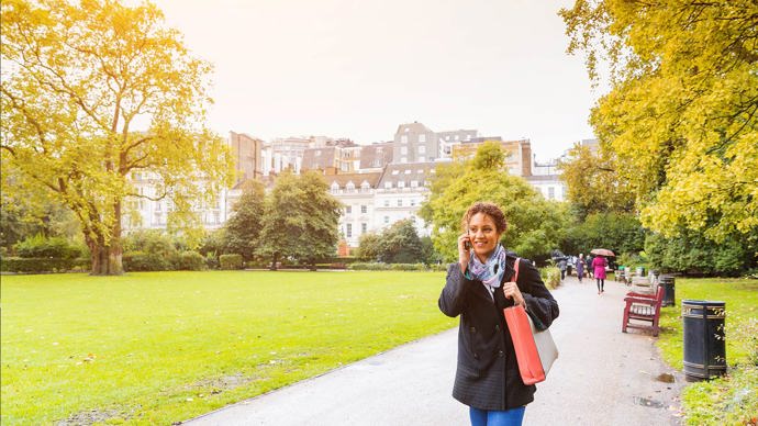 Young woman walking through a London park while talking on her mobile phone.
