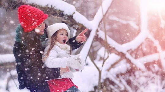 Smiling mother pointing something out to her excited daughter in a snowy forest