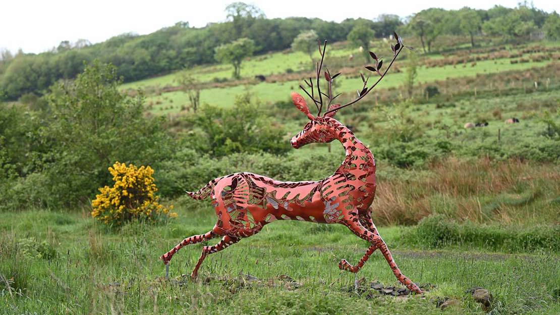Sculpture of a deer in grassland surrounded by trees