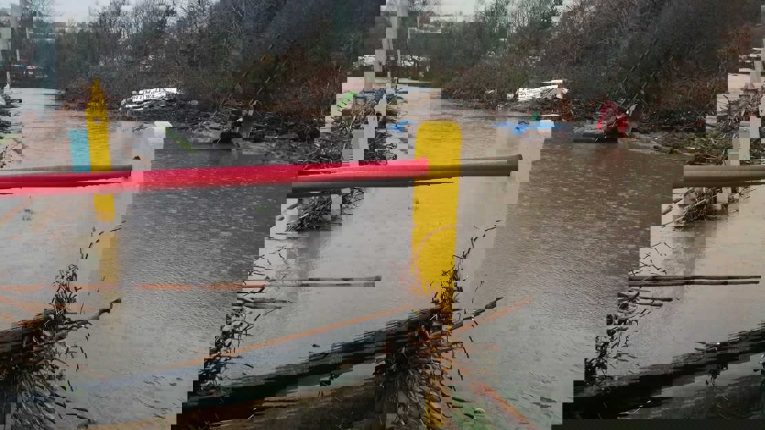 Rain falling on a river that has burst its banks and spread branches and debris around rugby pitch fencing and the opposite bank