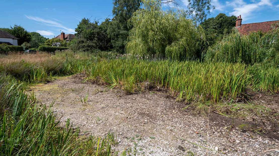 A dry village pond during the 2022 summer heatwave and drought, climate change consequences. Newnham village green, Hampshire.