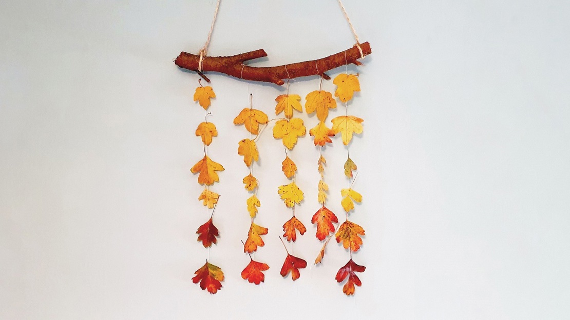 A small branch on a wall with lots of small colourful leaves hanging from it