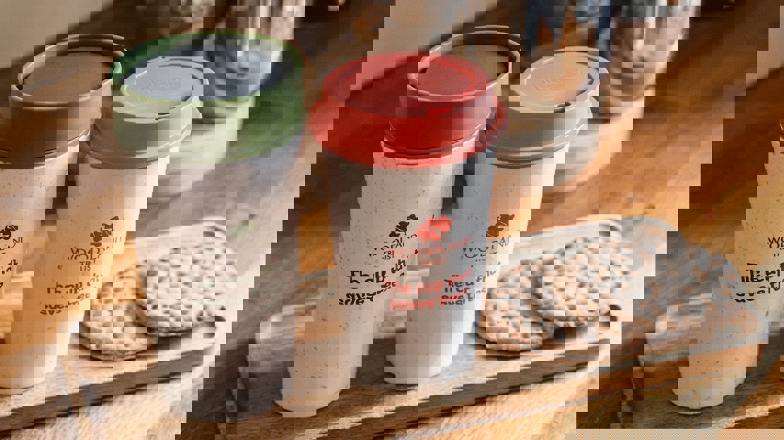 Two reusable insulated cups on a wooden tray with some biscuits