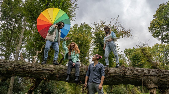 group of young people on log with rainbow umbrella