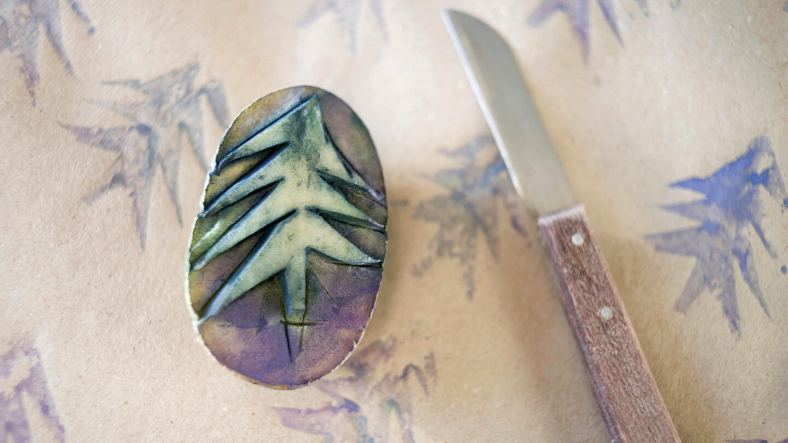 Christmas tree shape cut into a potato and printed onto paper behind