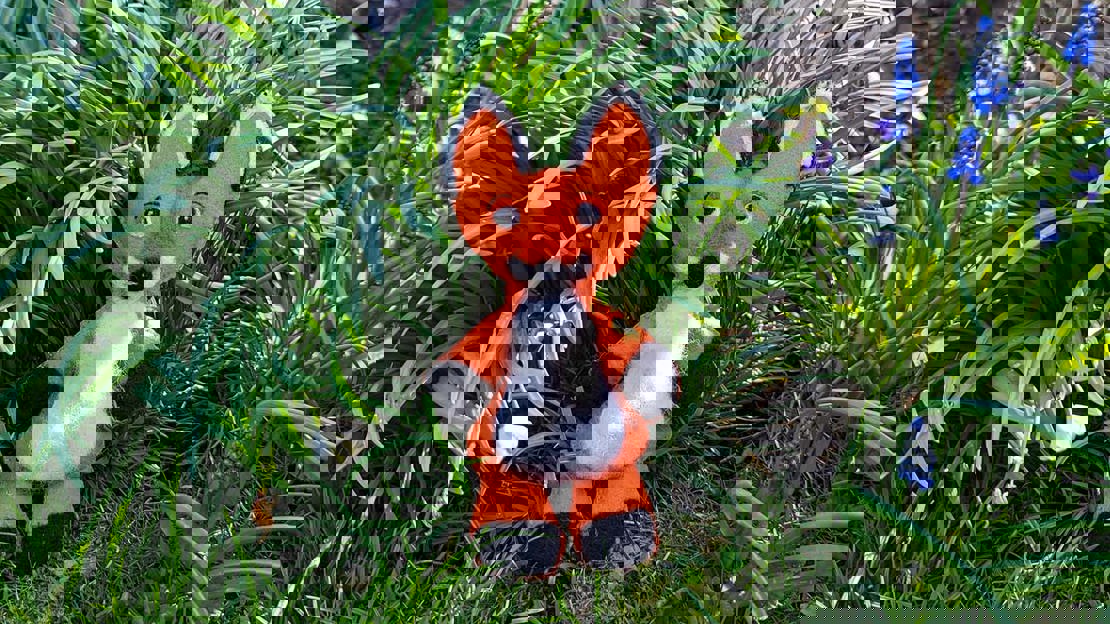 A finished felt fox sitting among plants in a garden