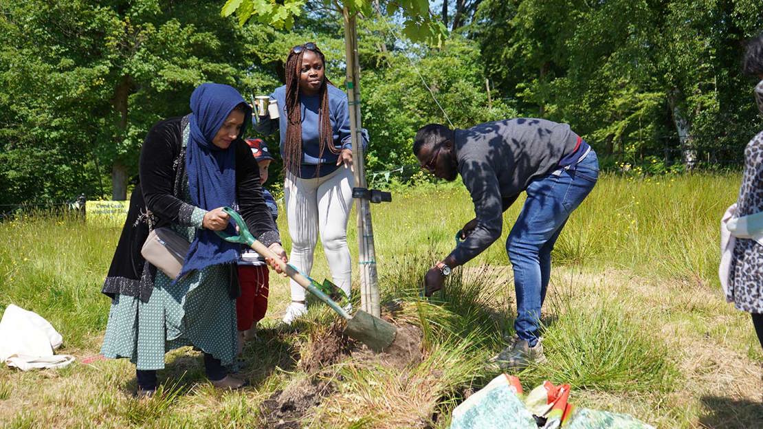 Three Windrush Elder family members planting a tree in the sunshine