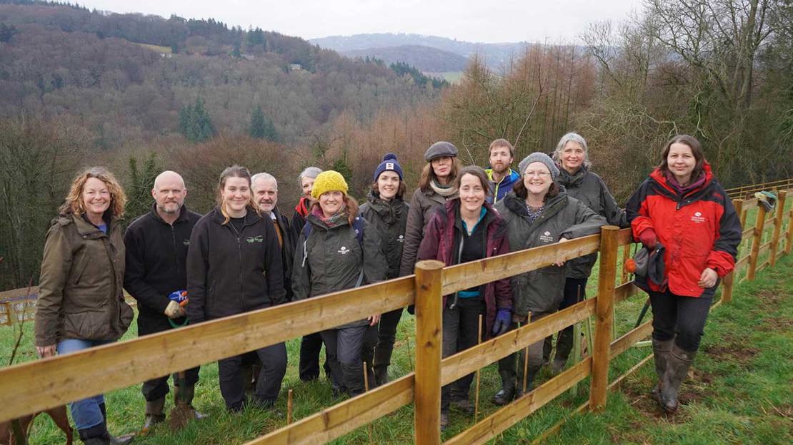 A group of Woodland Trust staff and Kate Humble standing behind a fence at the top of a sloping field