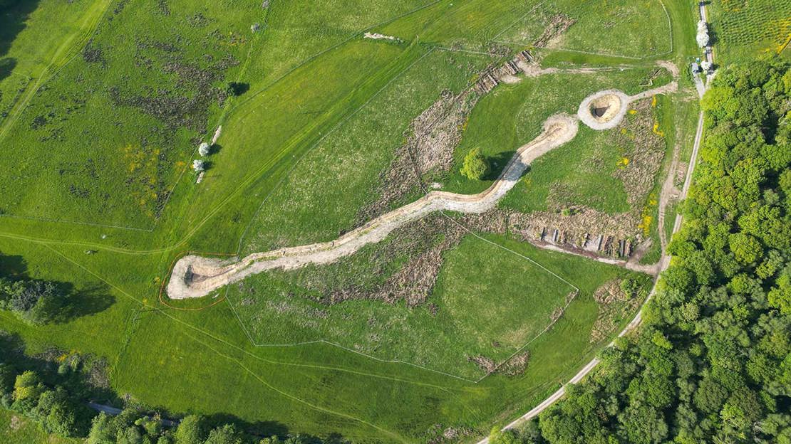 Aerial shot of a chalky white ditch dug into a green field surrounded by trees