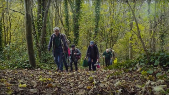 Group of volunteers walking through a wood with bags and tools