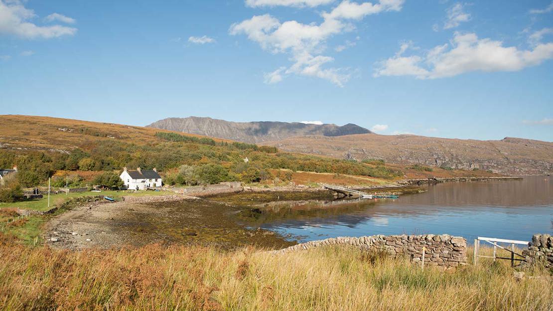 Trees and a house beside a remote Scottish loch on a blue sky day