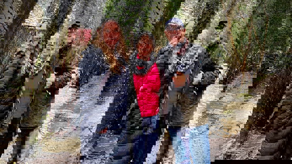 Three people in winter coats with a tree-lined river behind them