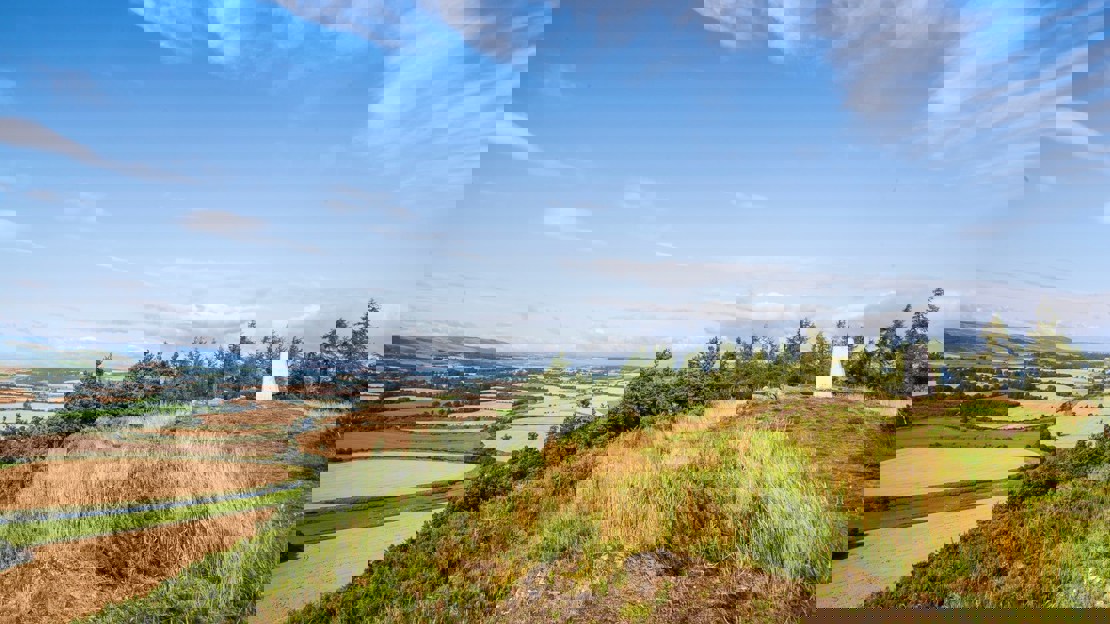 Grassy hilltop edged with stone remains and marked by a small white monument