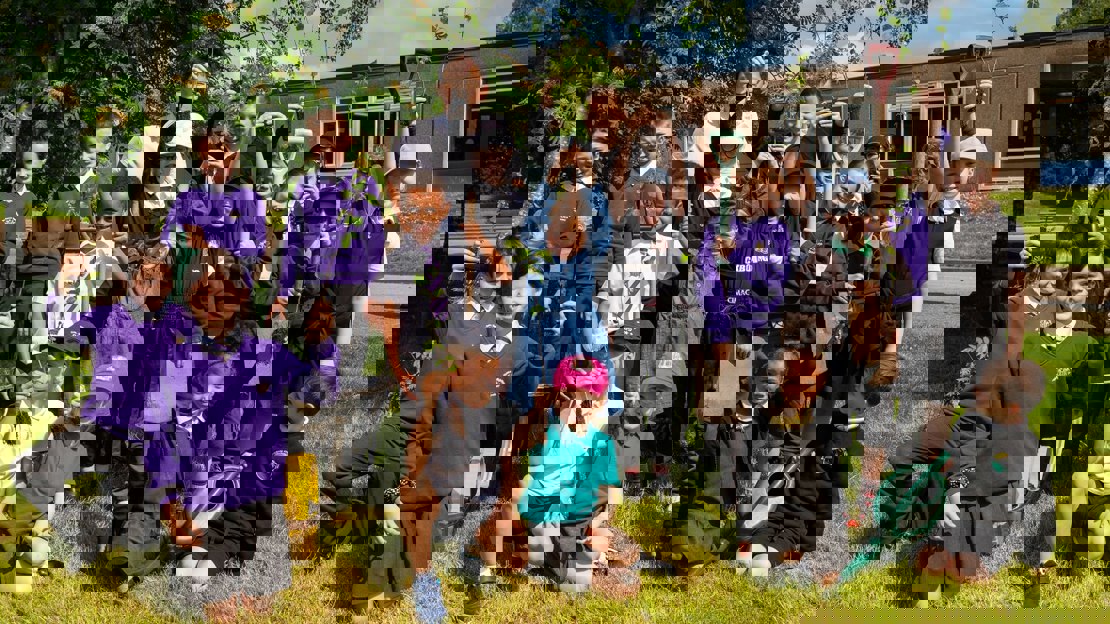 A group of schoolchildren holding saplings and planting equipment outside a school building A group of schoolchildren holding saplings and planting equipment outside a school building