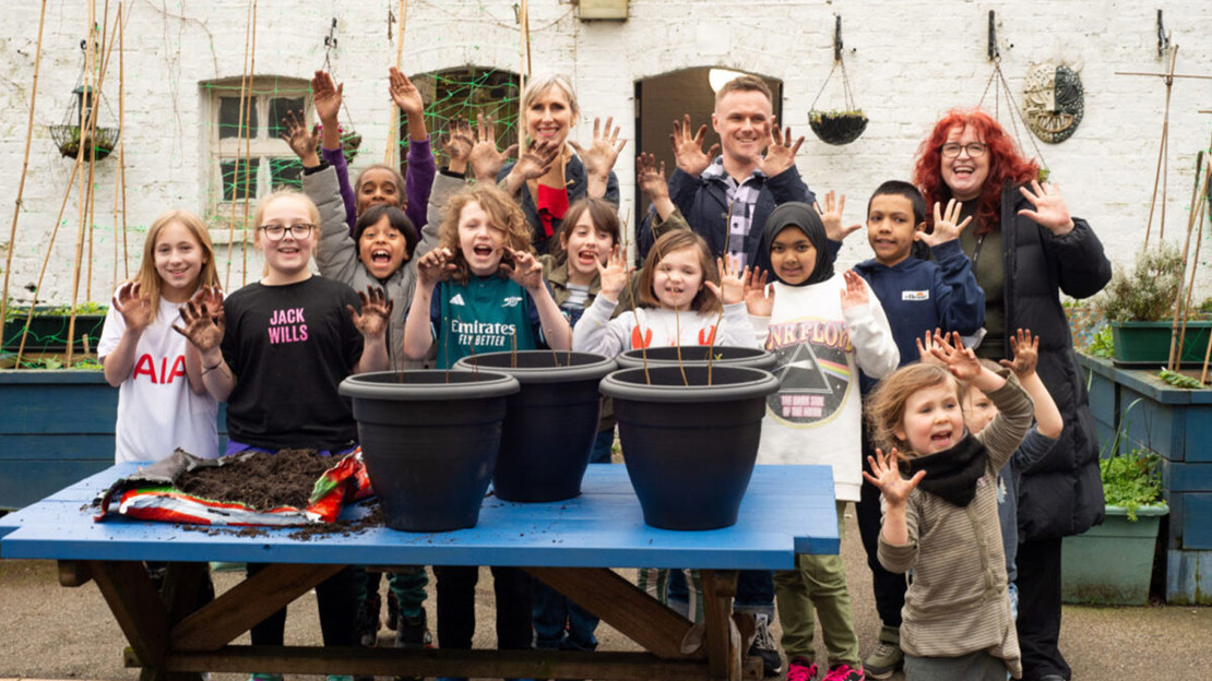 Author Lauren Child and school pupils standing behind plant pots and holding muddy hands up to the camera