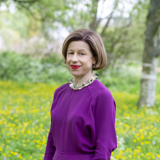 Head and shoulders shot of Woodland Trust trustee, Julia Knights, with a background of grassland and trees
