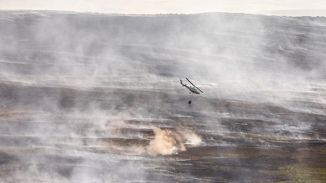 A firefighting helicopter dropping water on a smoking landscape.