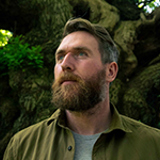 Luke Adam Hawker standing in front of a tree trunk