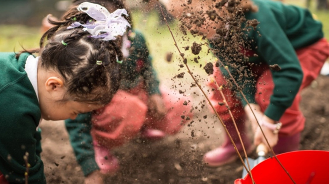 Children throwing soil while planting trees.