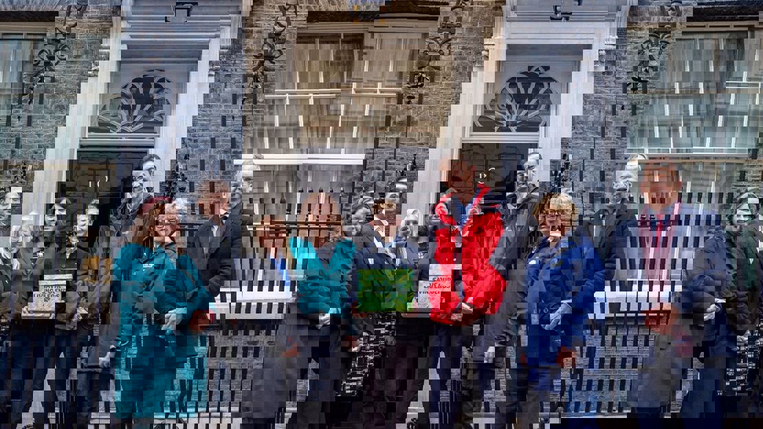 Eight people stand in front of 10 Downing Street with a green box that says 'save our living legends'