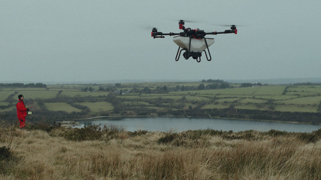 Drone in flight above moorland landscape with person in the distance.