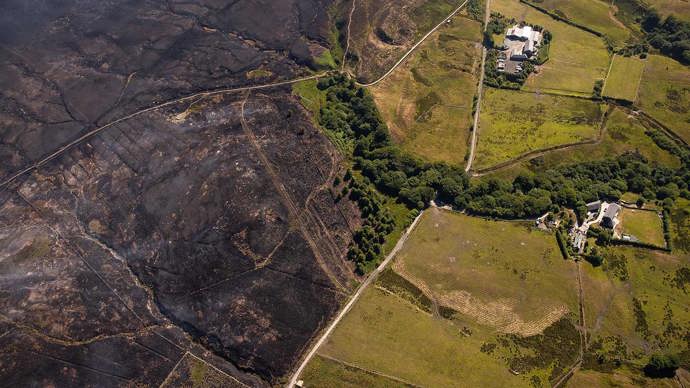 Arial shot looking down at landscape, with burnt area on one side and green, untouched land on the other side,