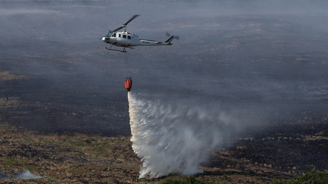 Helicopter dropping water on burning landscape.