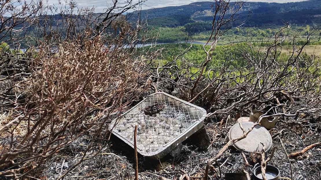 Used disposable barbecue sitting amongst burnt ground and vegetation.